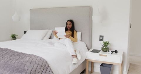 Young woman reading letter on minimalist bed in neutral contemporary bedroom
