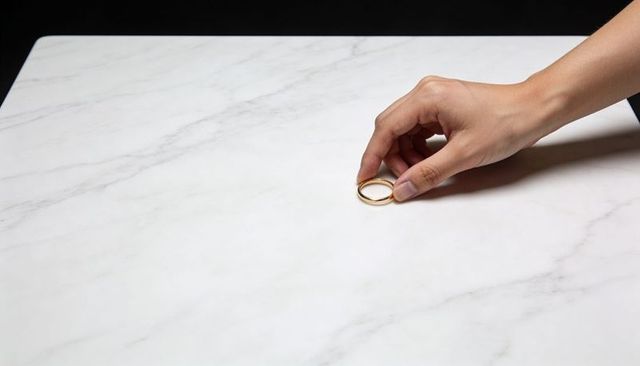 Closeup hand holding two gold wedding rings on marble tabletop minimalist jewelry concept