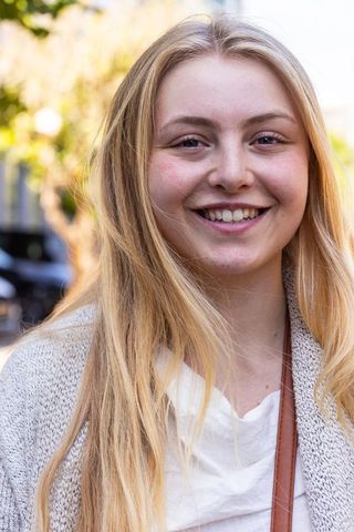 Young woman smiling on urban street wearing gray cardigan white top closeup portrait