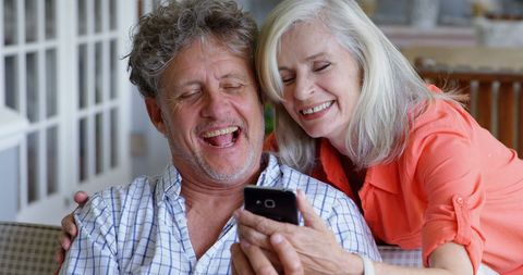 Senior Caucasian Couple Joyfully Engaging with Smartphone at Home