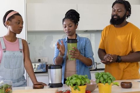Black family preparing green smoothie together in modern kitchen with fresh basil