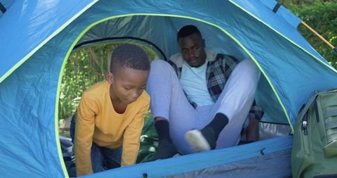 African american father and son camping in blue dome tent at sunlit woodland campsite bonding