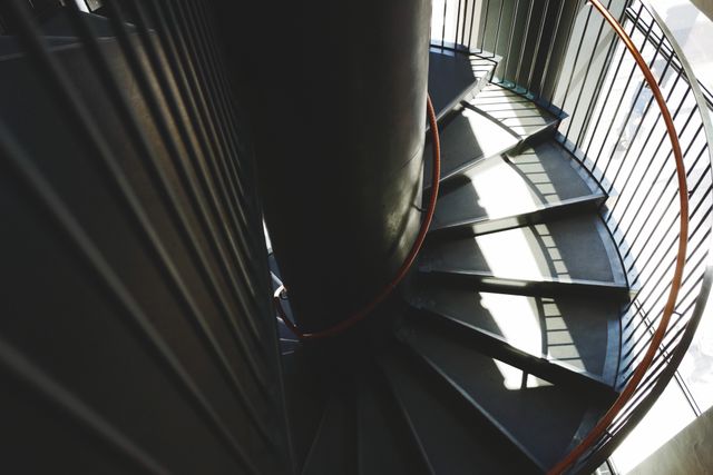 A modern spiral staircase inside an industrial building with metal railing and steps radiating around a central column. Suitable for articles or blog posts on architecture, urban development, or interior design themes. Could be used in architectural magazines, websites focusing on contemporary design, or promotional material for industrial space rentals.