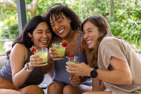 Friends toasting with green cocktails on patio sofa laughing and celebrating friendship
