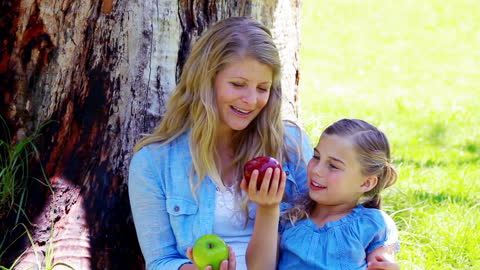 Mother and Daughter Sharing Apples Under Tree in Park