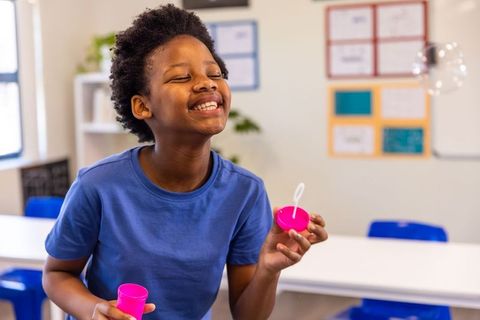 Joyful african american boy blowing bubbles in classroom playful learning moment
