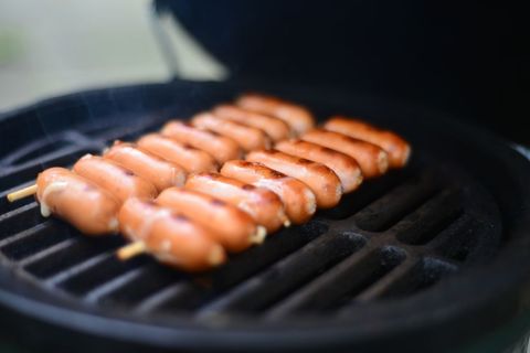 Grilling cocktail sausages on skewers over charcoal barbecue grill close-up