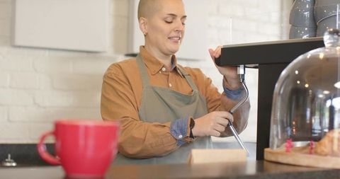 Female barista steaming milk at espresso machine in minimalist cafe with pastries