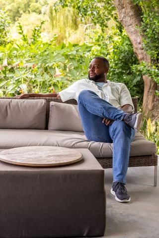African american man relaxing on rattan sofa in sunlit garden patio