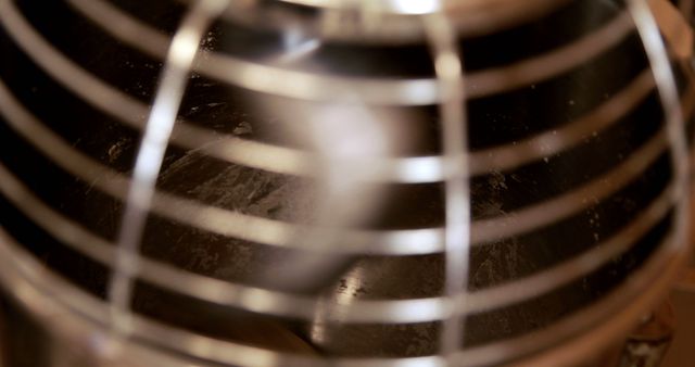 Close-up view of a metallic whisk attachment from a kitchen mixer, with copy space. It captures the detail and texture of the kitchen tool, emphasizing its role in food preparation and baking.