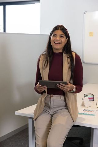 Smiling professional presenting with tablet while sitting on desk in bright modern office