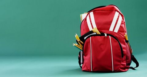 Red backpack filled with school supplies in classroom