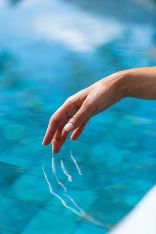 Woman fingertips skimming turquoise pool water creating gentle ripples and reflections