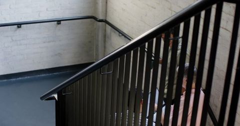 Two Friends Climbing Modern Staircase Against Brick Walls