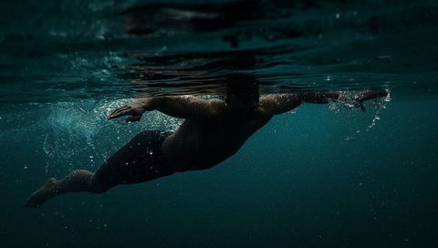 Male swimmer gliding just below surface in deep teal ocean with splashing bubbles