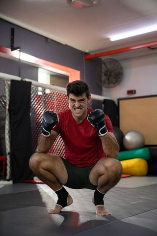 Squatting mma fighter clenching fists in gym training with intense determination