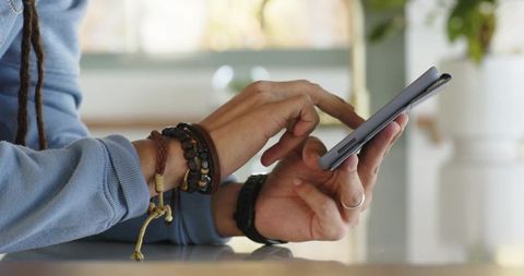 Mid 30s man tapping smartphone in folio case on glossy kitchen counter wearing bracelets