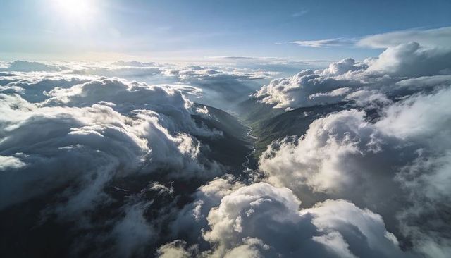 Soaring above dramatic cloud banks and sunlit mountain valley with winding river view