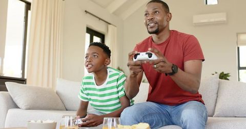 African american father and son playing video games on couch sharing joyful bond