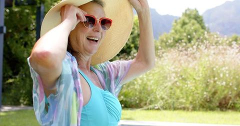 Smiling Elderly Woman with Straw Hat and Sunglasses Enjoys Sunny Day Poolside