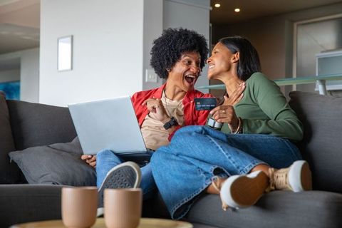 Diverse couple celebrating successful online purchase relaxing on couch