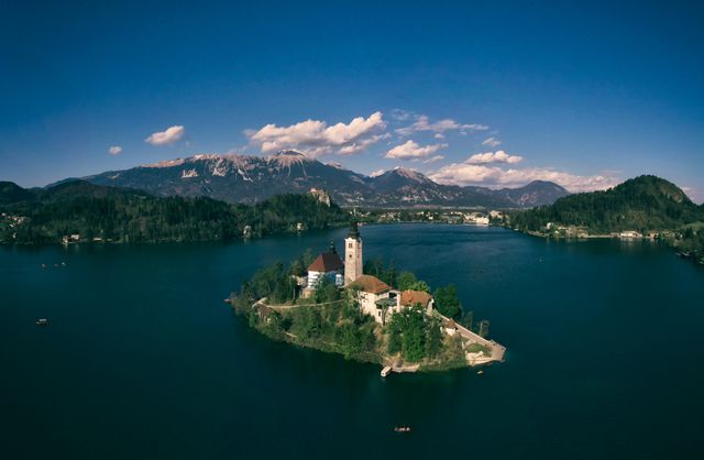 Capturing serene centerpiece beauty of Lake Bled, Slovenia, this image shows an aerial view of the famous island with its historic castle and church. Surrounded by clear blue waters and scenic mountains, it is perfect for travel promotions, nature articles, and European tourism campaigns.