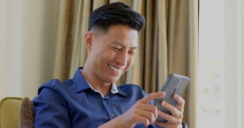 Asian man texting smiling indoors bright room