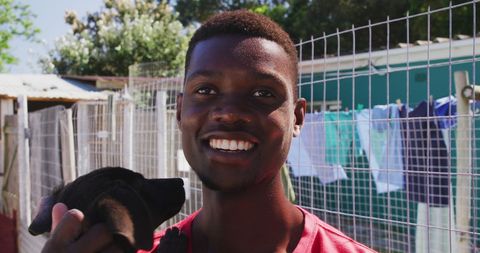 Smiling Man Holding Black Puppy at Dog Shelter Outdoors