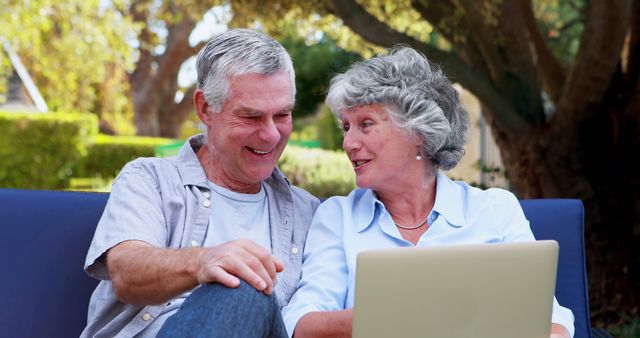 A senior Caucasian couple shares a joyful moment while looking at a laptop screen together, with copy space. Their interaction highlights the importance of technology in staying connected and engaged at any age.