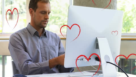 Man Working at Computer Surrounded by Heart Icons in Office