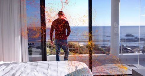 Midadult woman standing on balcony overlooking ocean with orange confetti in modern bedroom