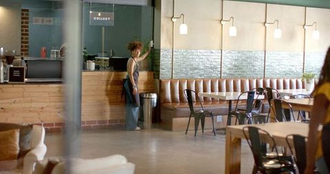 African american barista behind wooden counter in modern cafe with leather banquette