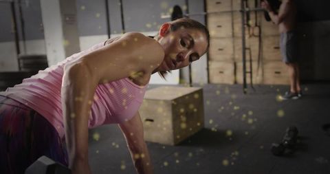 Female athlete performing bent-over dumbbell row in industrial gym with gritty dust effect