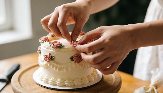 Hands Decorating Two-Tier Buttercream Cake with Rosette Piping on Wooden Board