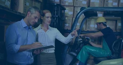 Co-workers discussing inventory management in warehouse with forklift