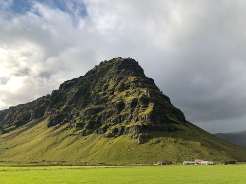 Dramatic Green Mountain Rising Above Icelandic Farmland Under Moody Storm Clouds