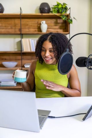 African american woman hosting podcast from minimalist home workspace with laptop microphone