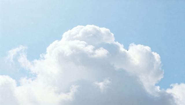 Sunlit Cumulus Cloud Billowing Over Pale Blue Sky with Soft Highlights and Wispy Edges