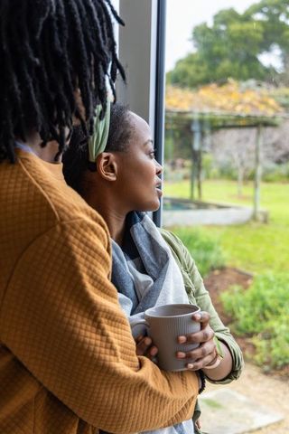 Couple embracing at window while enjoying coffee overlooking garden pergola