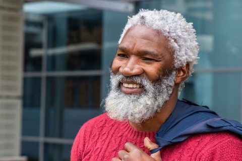Confident smiling senior man wearing red knit sweater and carrying navy jacket outdoors