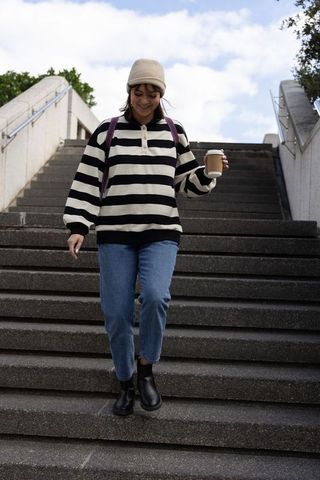 Young woman walking down urban stairs holding coffee cup and backpack, casual street style