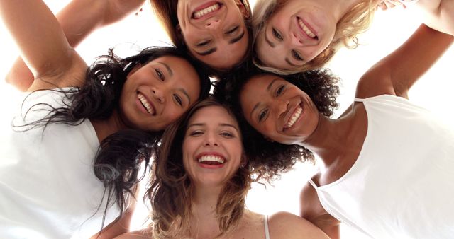 Group of smiling women of different ethnicities forming a close circle with heads together. They are sharing a joyful moment and demonstrating unity and happiness. Ideal for illustrating concepts of friendship, diversity, teamwork, female empowerment, and bonding activities. Suitable for use in marketing materials, social media campaigns, and community engagement initiatives.