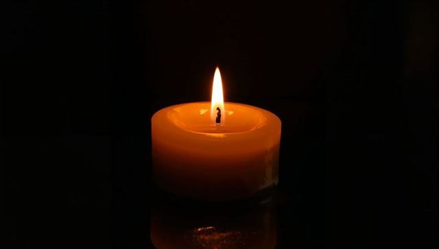 Flickering Amber Votive Candle Casting Warm Glow and Reflection on Glossy Black Surface