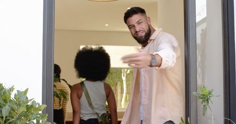 Man welcoming friends into modern home with open door