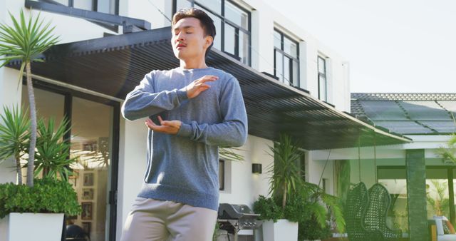 Image of relaxed biracial man exercising tai chi in garden. leisure, relax, active lifestyle and spending free time at home and garden concept.