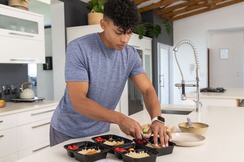 Young african american man preparing healthy meal-prep containers on kitchen island