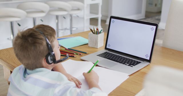 Happy caucasian boy during online school lesson using headset and laptop, copy space on screen. online education at home.