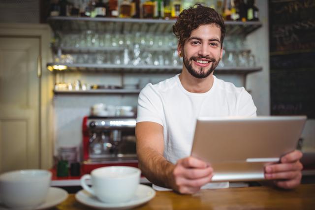 Portrait of smiling waiter using digital tablet at counter in cafÃ©