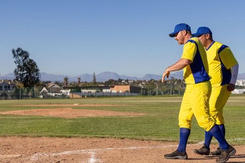 Veteran Baseball Teammates Walking Baseline in Yellow Blue Uniforms on Sunny Diamond