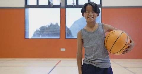 Asian Boy Smiling Holding Basketball on Indoor Court